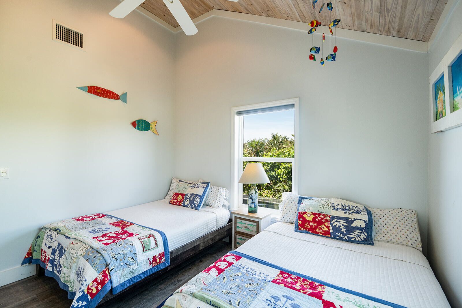 A bedroom with two beds, a window with a view, and decorative fish on the wall.