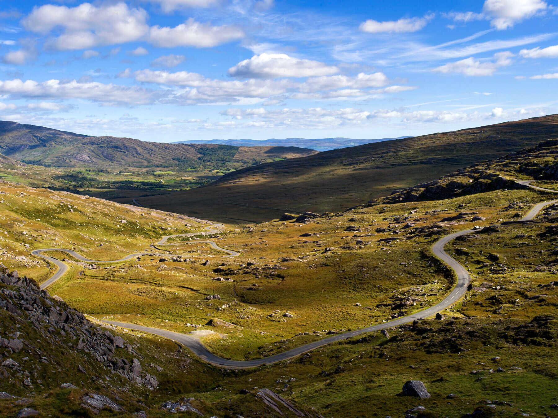 A winding mountain road through a valley with rocky terrain and sparse vegetation.