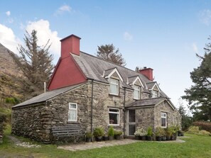 Traditional stone house with a red-tiled roof, surrounded by a well-maintained lawn and potted plants.