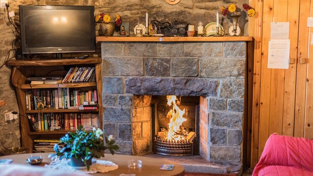 A cozy living room with a stone fireplace, a television, and a bookshelf filled with books. - Angelas Farmhouse (Lauragh)