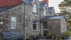 A stone house with a red roof, a bench, and potted plants. - Angelas Farmhouse (Lauragh)
