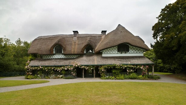 A traditional house with a thatched roof, a green garden, and a paved driveway. - Garden Cottage (Clogheen)