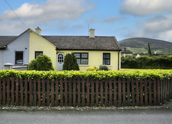 A two-story house with a yellow facade, a dark roof, and a wooden fence in front. - Garden Cottage (Clogheen)