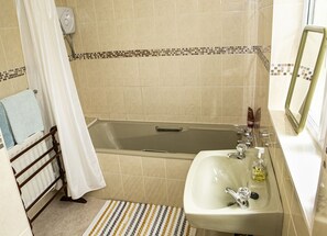 A bathroom with a bathtub, a sink, and a showerhead. - Garden Cottage (Clogheen)