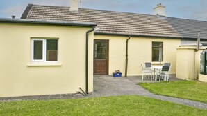 A small, single-story house with a tiled roof, a front door, and a small patio area with a table and chairs. - Garden Cottage (Clogheen)
