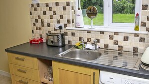 A kitchen with a sink, a toaster, a dish rack, and a window with a view of greenery. - Garden Cottage (Clogheen)