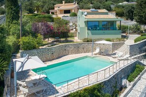 A swimming pool with stone walls and lounge chairs, surrounded by a stone wall and greenery. - Kalami Beach - Villa Almyra (Corfu)