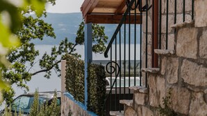 Ein Steinhaus mit einem hölzernen Balkon und Metallgeländer mit Blick auf ein Gewässer.