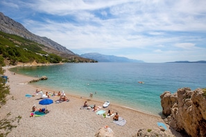 A beach with people sunbathing, a clear sky, and mountains in the background.