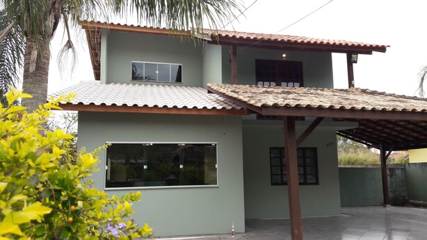 A two-story building with a tiled roof, large windows, and a covered patio area. - Cozy in Floripa (Florianópolis)