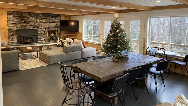 Un vaste espace de vie agrémenté d’une cheminée en pierre, d’une grande table à manger en bois et d’un sapin de Noël.
