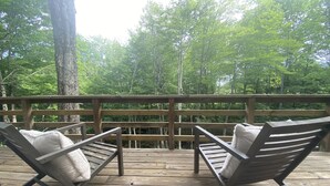 Une terrasse en bois avec deux chaises longues et une table, entourée d’arbres.