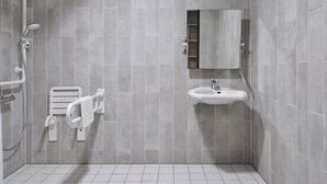 A modern bathroom with grey tiles, a white sink, a mirror, and a shower area. - B&B Hotel Mannheim-Neuostheim (Mannheim)