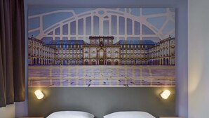 A hotel room with a large bed, two bedside tables, and a wall-mounted artwork of a building. - B&B Hotel Mannheim-Neuostheim (Mannheim)