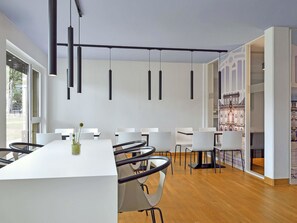 A modern conference room with a long table, white chairs, and pendant lighting. - B&B Hotel Mannheim-Neuostheim (Mannheim)
