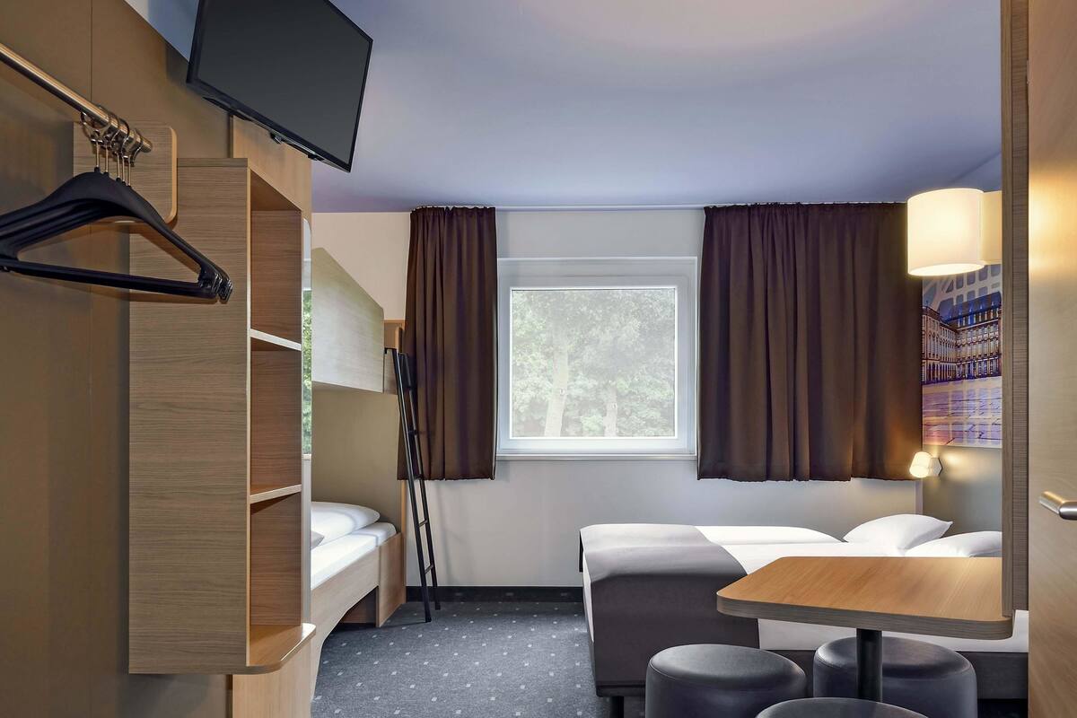 Quarto de hotel pequeno com uma cama beliche, uma escrivaninha e uma cadeira.