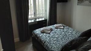 Une chambre à coucher avec un lit, un bureau, une fenêtre et un tableau accroché au mur.