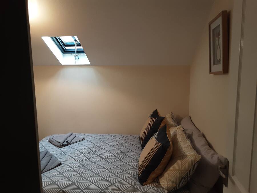 A bedroom with a skylight, patterned bedspread, and multiple pillows.