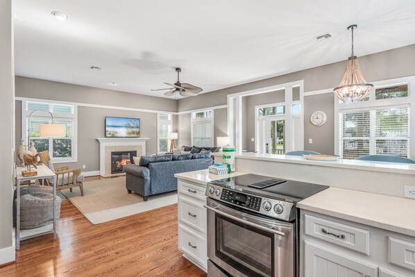 A modern kitchen with a built-in oven, a dining area with a table and chairs, and a living room with a sofa and fireplace.