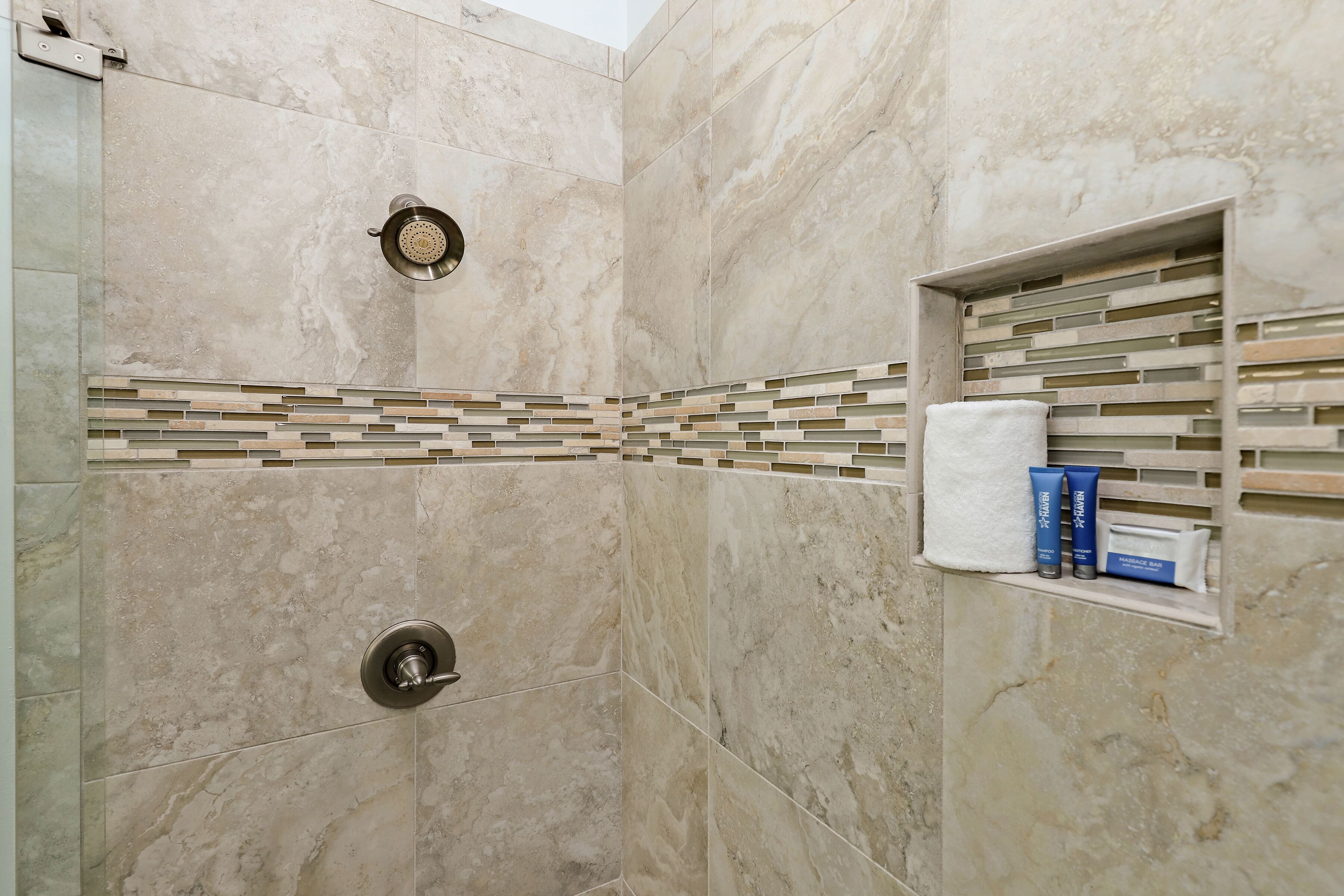 A bathroom with a shower, tiled walls, a towel rack, and toiletries.