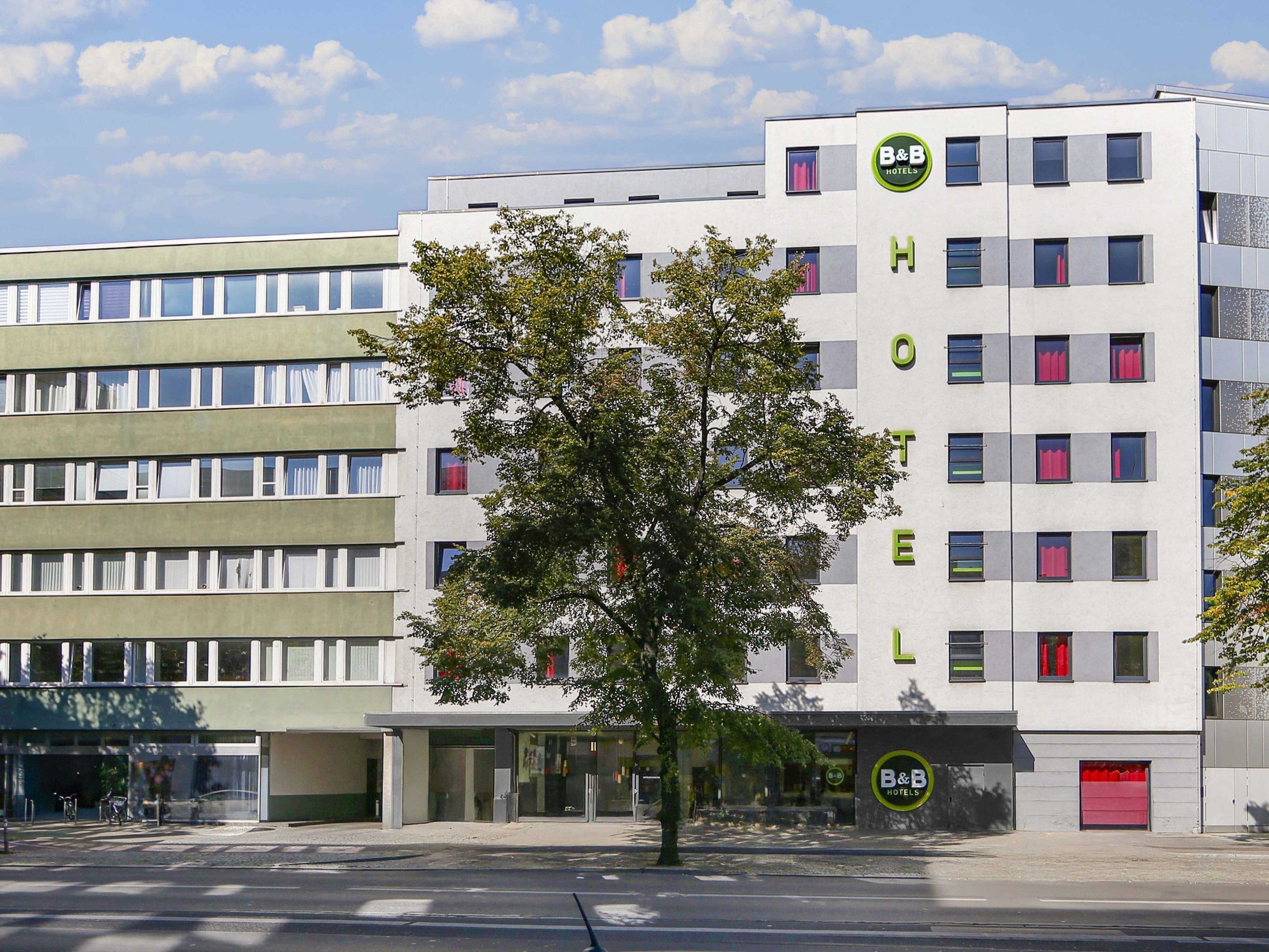 Un hotel moderno con un llamativo logotipo de B&B, varios pisos y un árbol en primer plano.