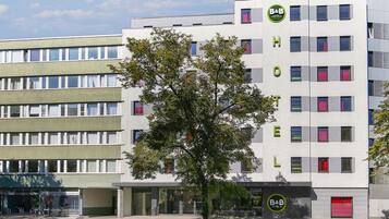 Un hotel moderno con un llamativo logotipo de B&B, varios pisos y un árbol en primer plano.
