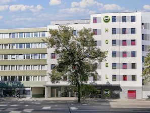 Ein modernes Hotelgebäude mit einem gut sichtbaren B&B-Logo, mehreren Etagen und einem Baum davor.