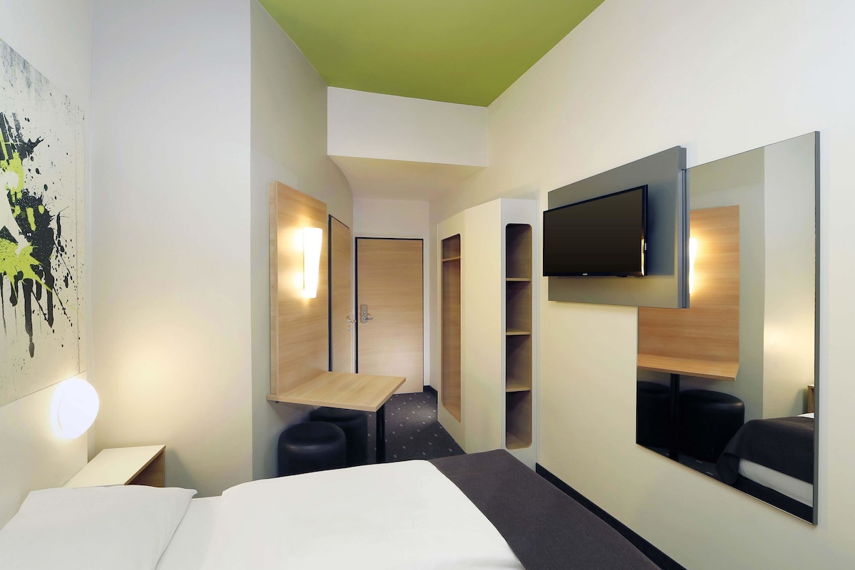 Ein modernes Hotelzimmer mit Bett, Schreibtisch, Fernseher und Kleiderschrank.
