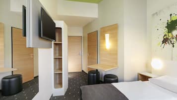 A modern hotel room with a bed, a flat-screen TV mounted on the wall, a small desk, and a wall-mounted light fixture.