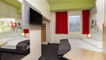 Habitación de hotel con dos camas, televisor, mesa y ventana con cortinas rojas.