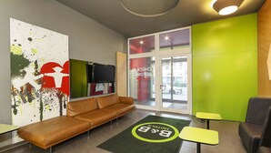 Un hall d’hôtel moderne avec un canapé en cuir, un comptoir d’accueil et un mur d’accent vert.
