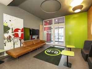 Een moderne hotel lobby met een leren bank, een receptiebalie en een groene accentmuur.