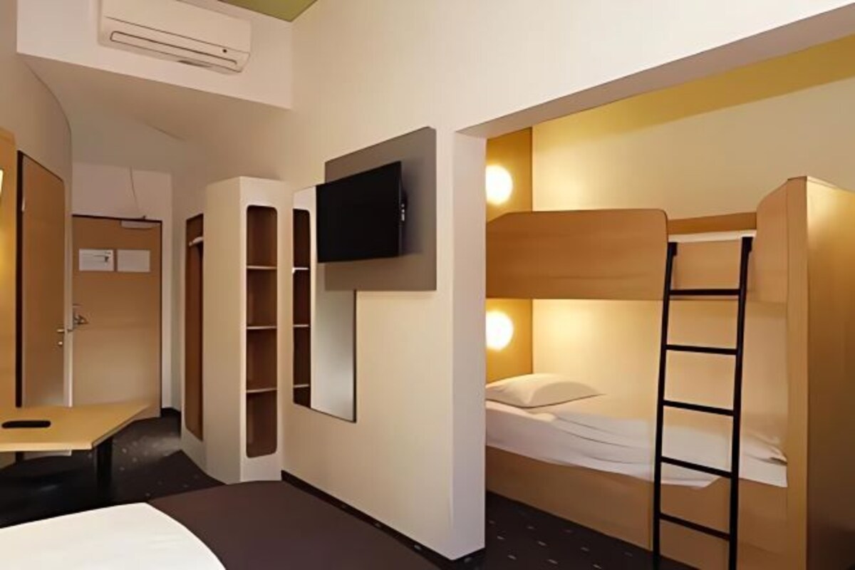 Een kleine hotelkamer met een stapelbed, een bureau, een aan de muur bevestigde televisie en inbouwplanken.