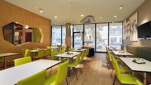 A modern restaurant interior with wooden flooring, green chairs, and tables.