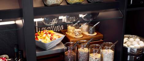 Een buffetgedeelte met verschillende soorten eten, waaronder een kom fruitsalade, potten met noten en zaden, en een kom rode bessencompote.