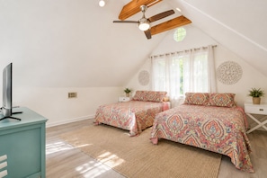 Ein Schlafzimmer mit zwei Betten, einem Deckenventilator, einem Fernseher und einem Fenster mit Vorhängen.