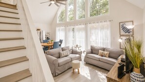 A spacious living area with a staircase, a ceiling fan, and large windows allowing natural light. - Lake-Front - Hot Tub, Large Dock, Fire Pit, Deck (Roxboro)