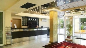A hotel lobby with a reception desk, a clock, and a large window. - Nikea Park (Varna)