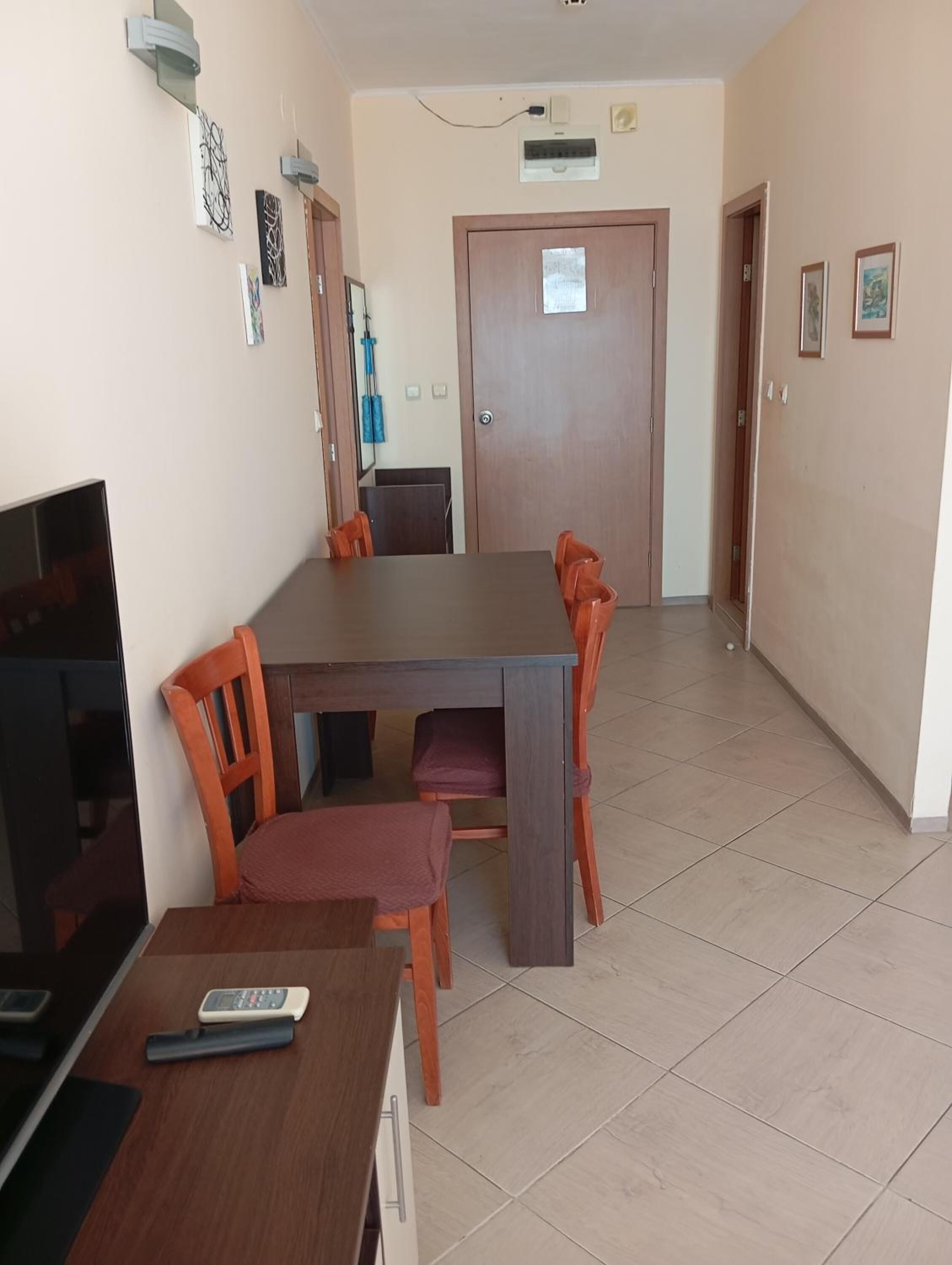 Un coin repas avec une table et des chaises en bois, un téléviseur et une télécommande posée sur la table.