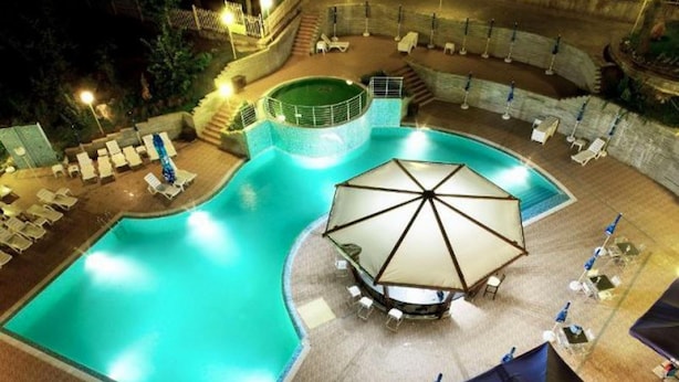 A swimming pool with lounge chairs and umbrellas, surrounded by a stone deck and a small waterfall feature. - Nikea Park (Varna)