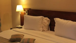 A hotel room with a neatly made bed, striped pillows, a bedside lamp, and a wooden headboard. - Nikea Park (Varna)
