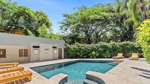 A swimming pool with a unique shape, surrounded by wooden lounge chairs and a concrete deck. - El Cometa. Walk to the beach! (Tamarindo)
