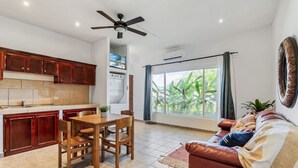 A modern living room with a brown leather sofa, a wooden dining table, and a kitchen area with wooden cabinets. - El Cometa. Walk to the beach! (Tamarindo)
