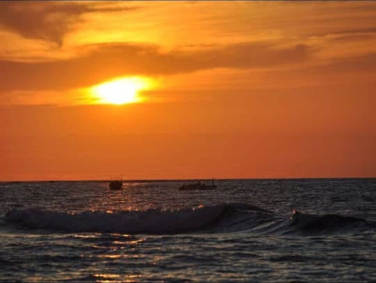 Un atardecer sobre el océano con olas y un barco a lo lejos.