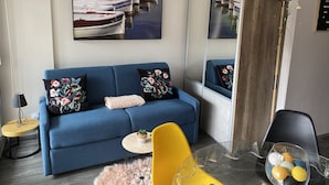 Un salon moderne avec un canapé bleu, un fauteuil jaune, une table en verre agrémentée d’objets décoratifs et un grand miroir qui reflète la pièce.