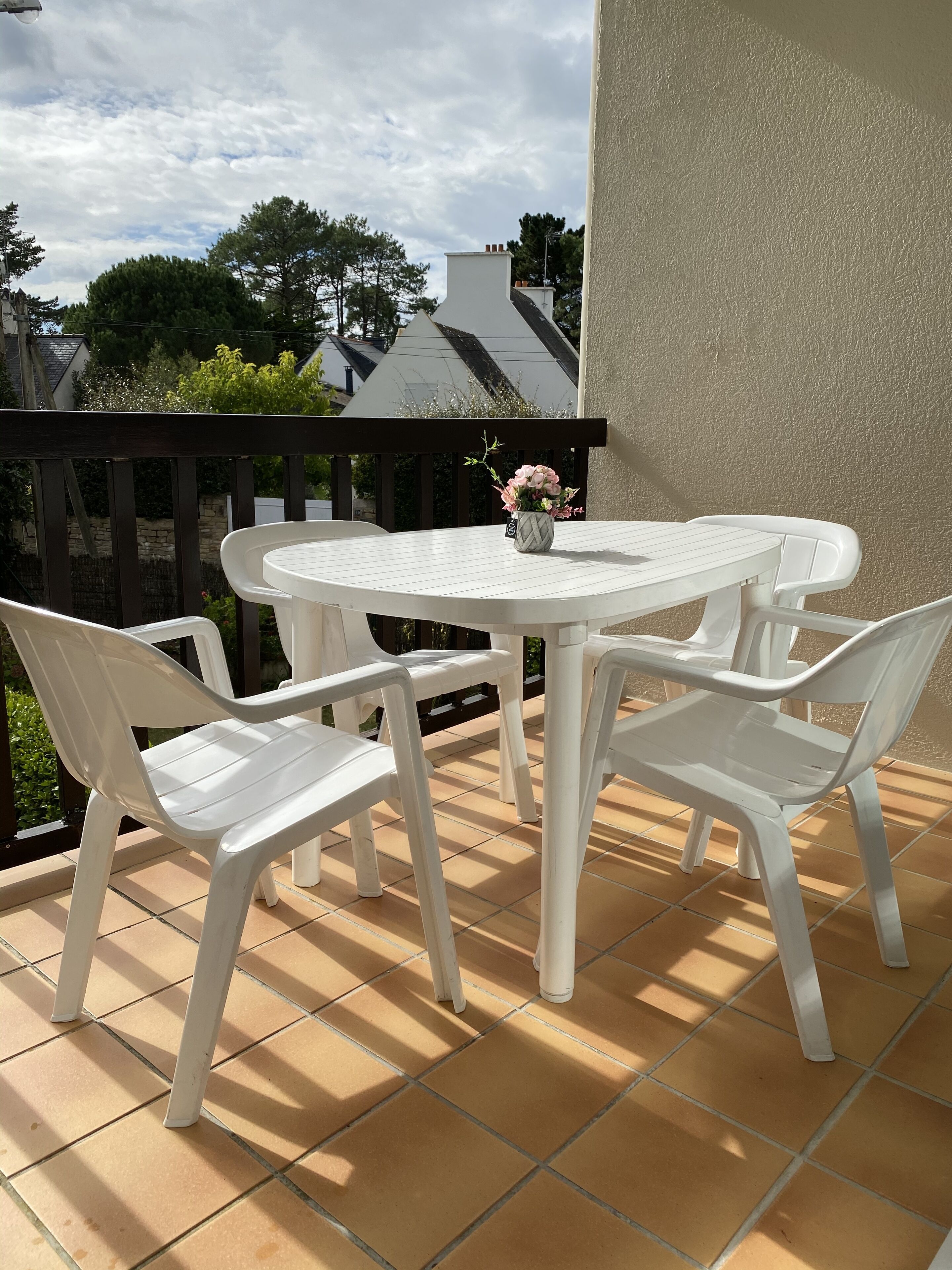 A round white table with two white plastic chairs on a tiled patio. A small vase with flowers is on the table.
