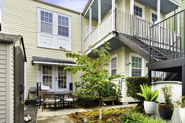 A two-story building with a covered patio, outdoor seating, and a small tree.