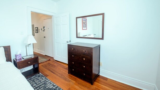 A bedroom with a bed, bedside table, lamp, dresser, and a door leading to another room. - Creole Cottage, Designer, Balcony (New Orleans)