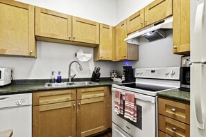 A kitchen with wooden cabinets, a stainless steel sink, a stove, and a coffee maker. - Creole Cottage, Designer, Balcony (New Orleans)