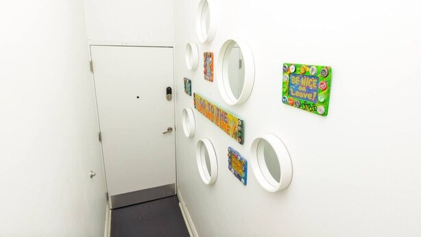 Un pasillo con una puerta blanca, un piso negro y varios espejos circulares en la pared.